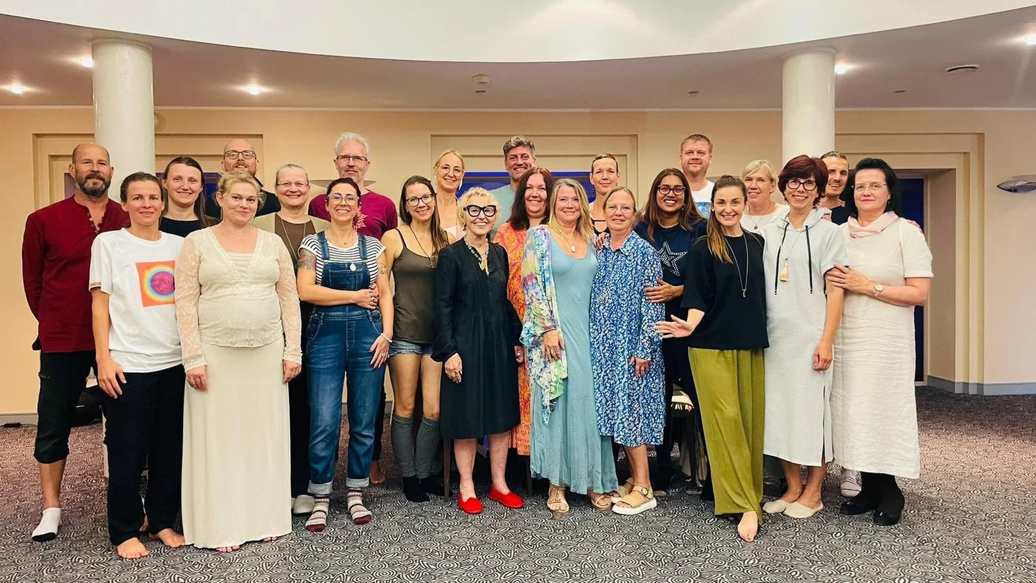 Group of 20 people standing together indoors, smiling for the photo.