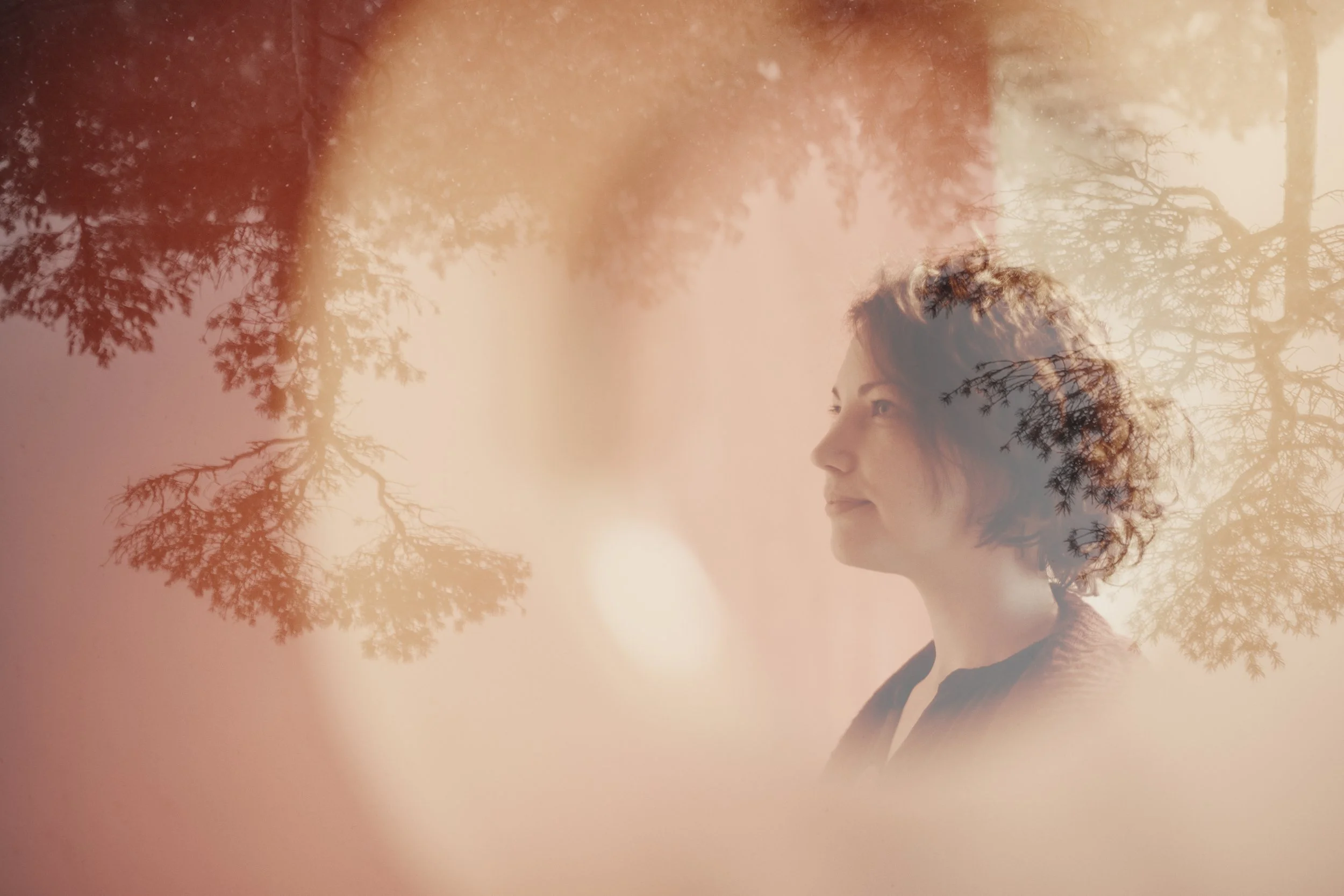 A woman with curly hair looking to the side, superimposed over a soft pink background with tree branches and leaves.
