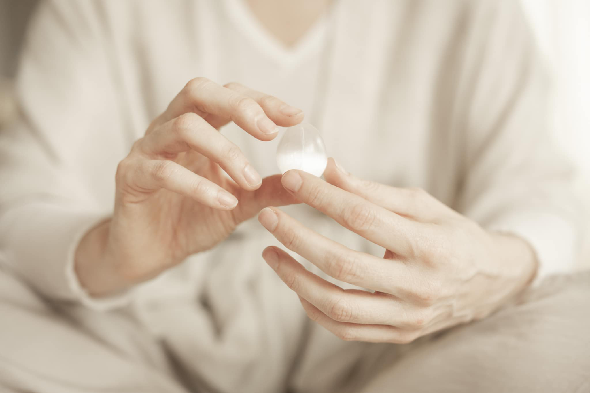 Close-up of person holding a transparent gel capsule pill between fingers.