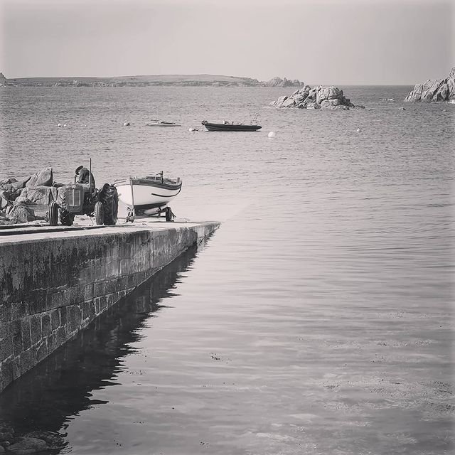 A black and white photo of a vintage tractor towing a punt up the quay