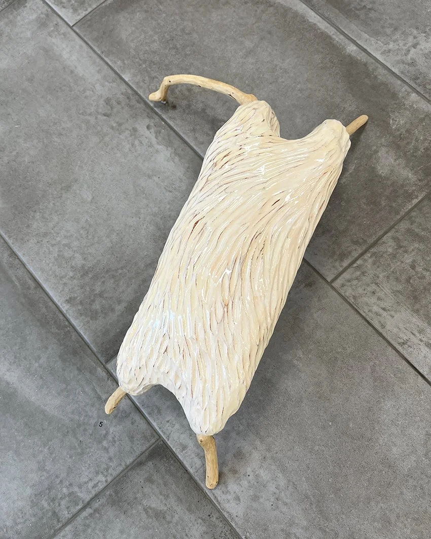 En konstgjord fåretavla med vitt ullhår och träben, placerad på ett grått klinkergolv.