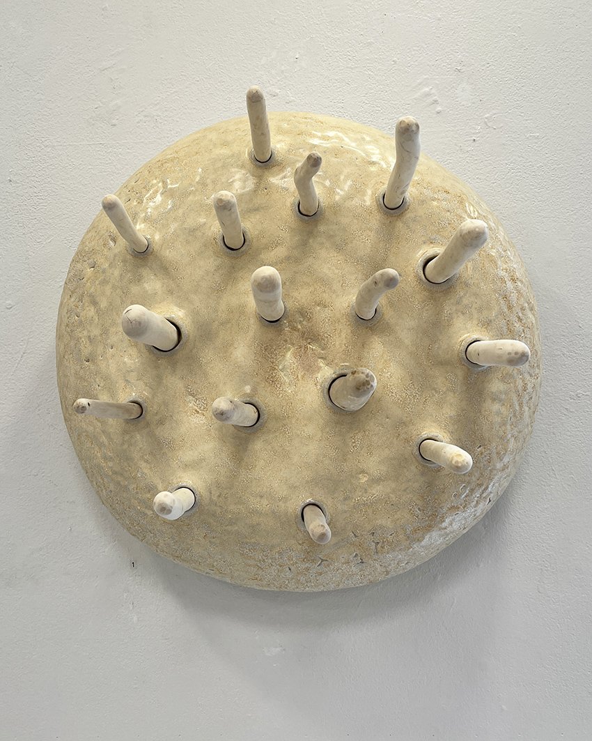 Skulptur som liknar en rund, beige sten med vita fingerliknande utskott över hela ytan.