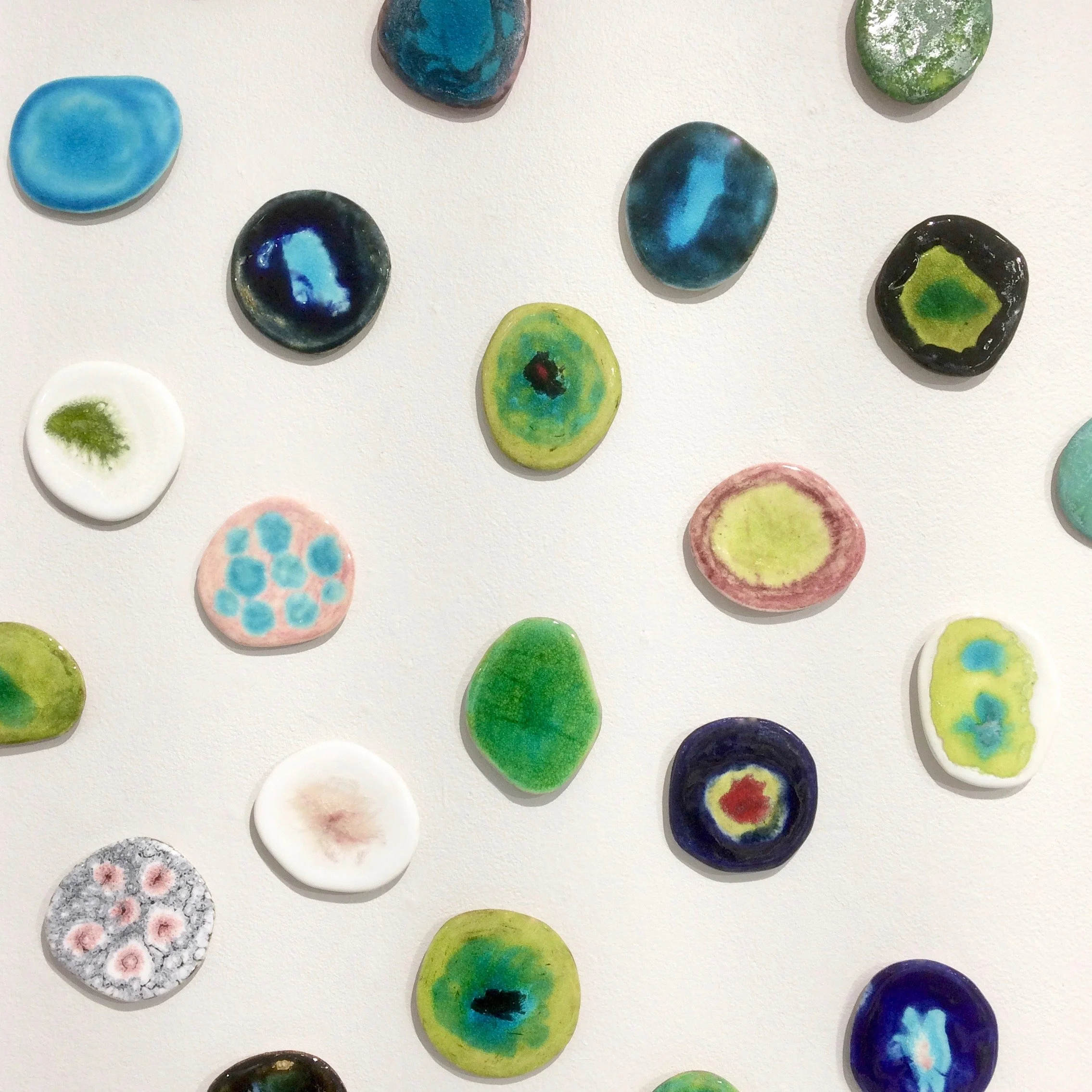 Färgglada, små glasplattor med olika mönster och färgskiftningar, arrangerade på en vit yta.