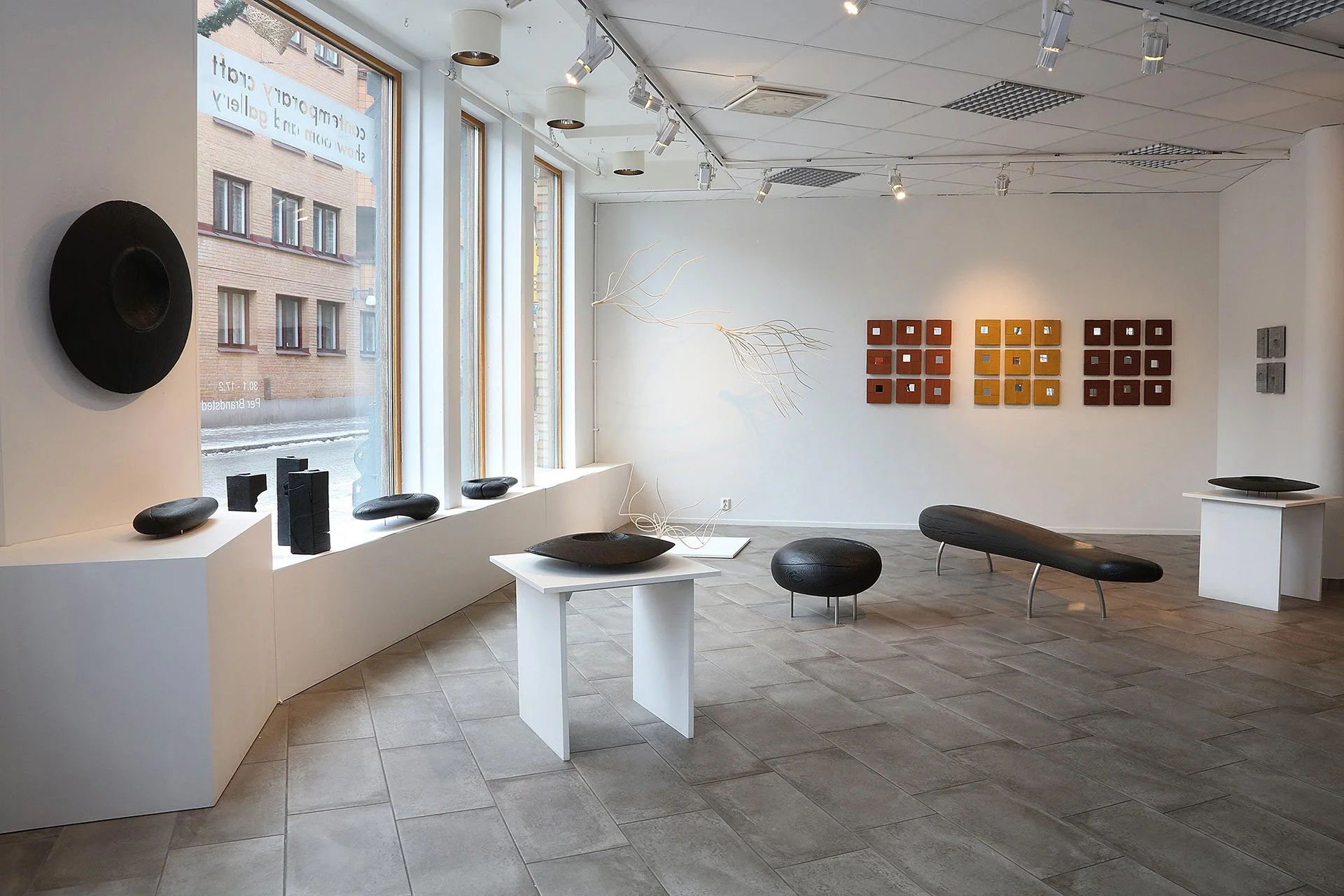 Konstgalleri med svarta skulpturer, färgglada konstverk på väggar och moderna möbler på golvet.