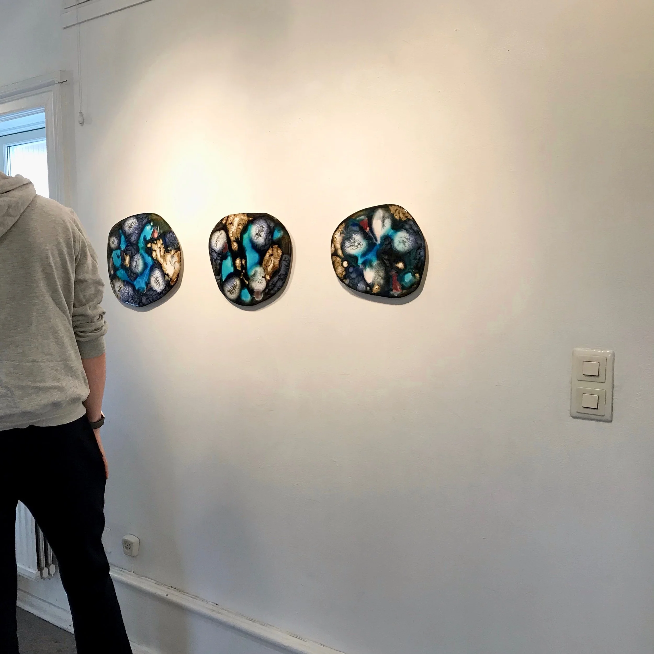 Tre konstverk på en vit vägg med en person till vänster och en väggkontroll på höger sida.