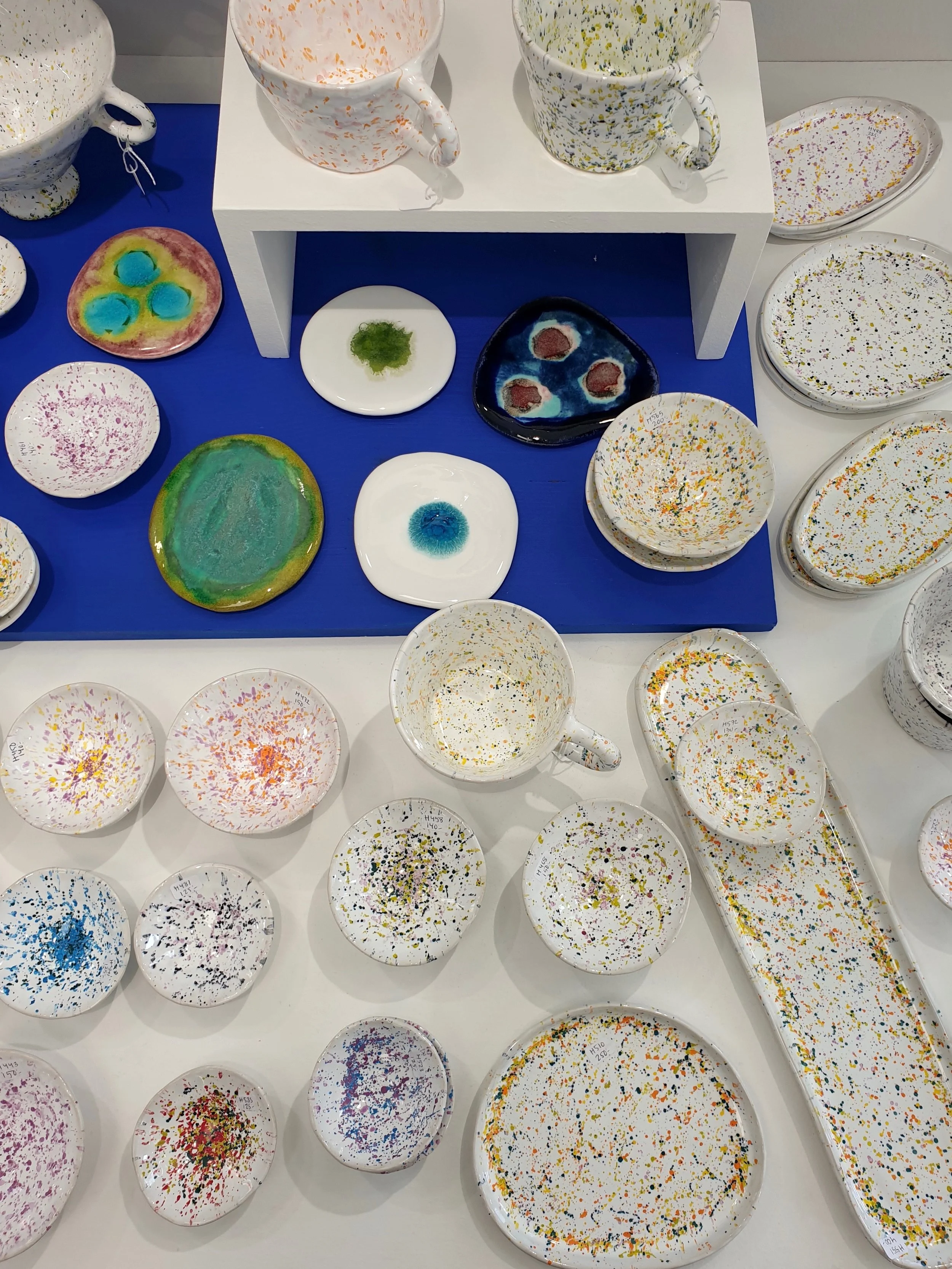 Färgade keramiska koppar, tallrikar och skålar med färgglatt, abstract mönster på en butiksyta.