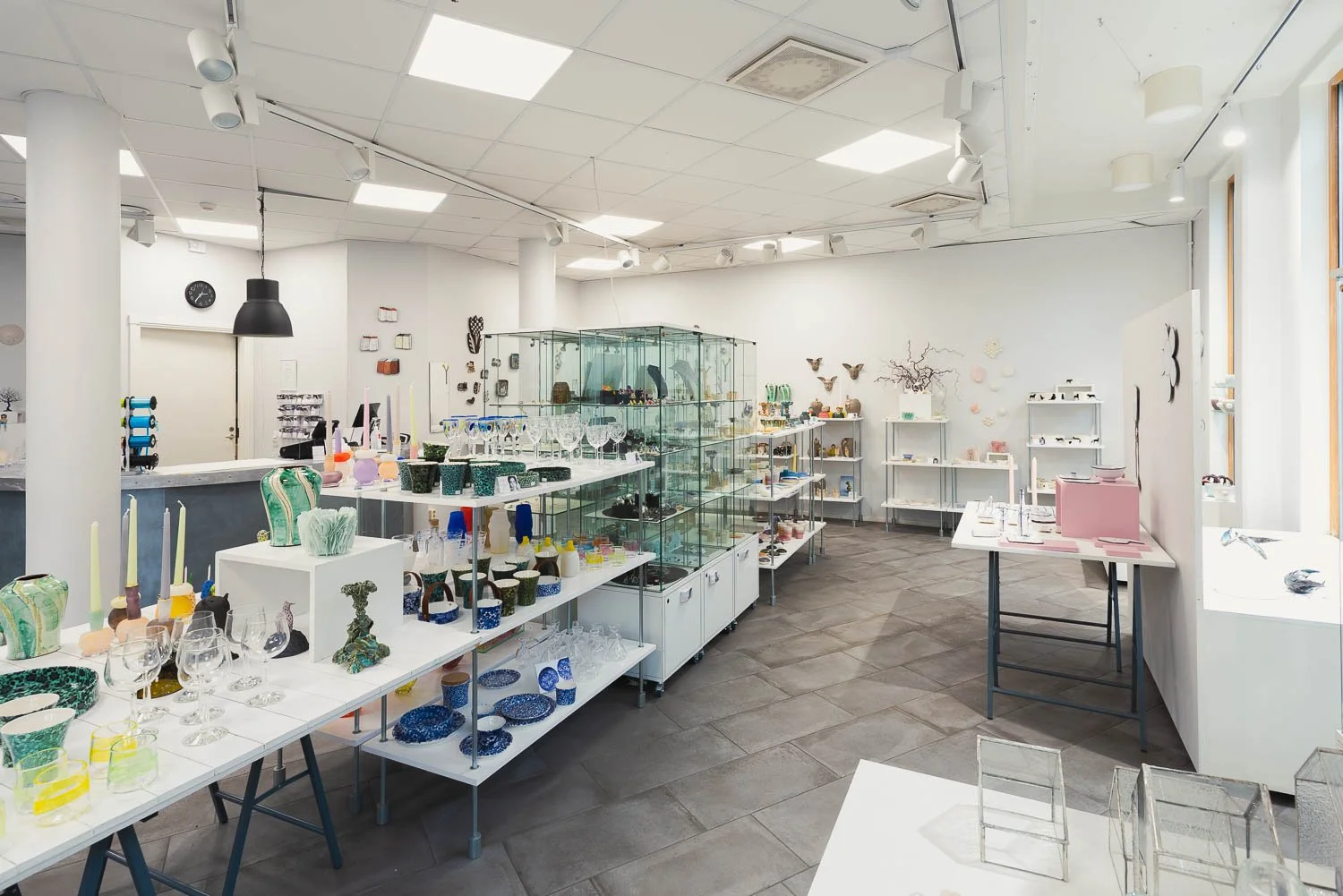 Inne i en butik som säljer glas, keramik och hantverk, med hyllor och bord fyllda med olika konstverk och prydnadsföremål.