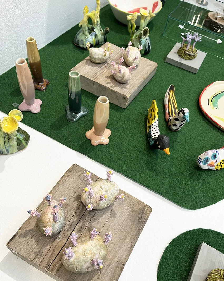 Ett bord med konstverk av uppstammade grönsaker, vissa med små rosa blommor, och dekorativa figuriner av fåglar och andra djur, samt vaser och andra dekorativa objekt.