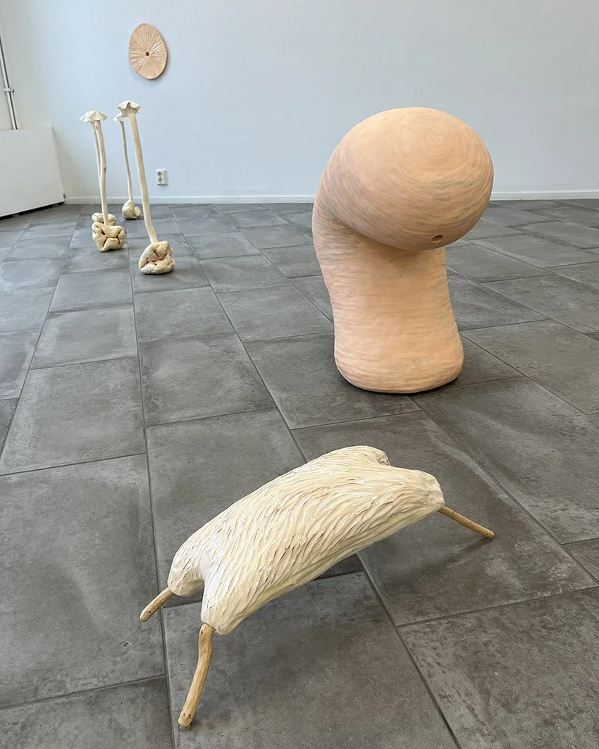 Skulpturer i ett konstgalleri, inklusive ett stort roterygghuvud, en långbent figur med vita ben, och en liten rovfågel i trä.