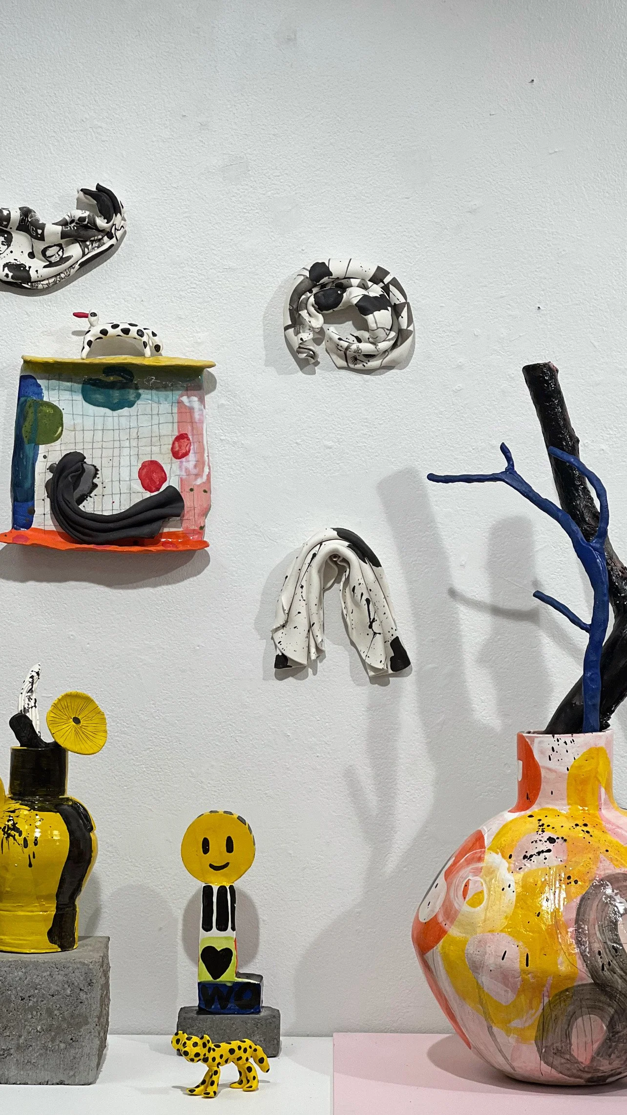 En konstutställning med trendiga och färgglada keramiska skulpturer och dekorativa föremål på en vit vägg och vit bord.