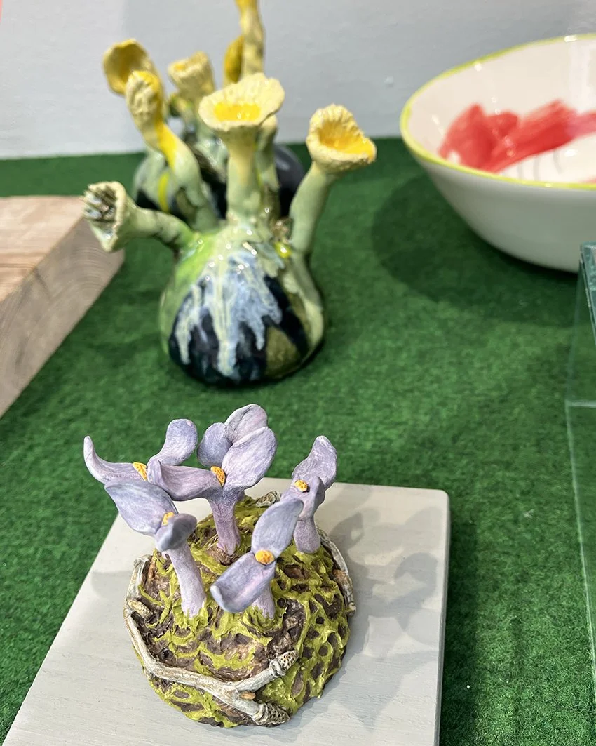 Två konstgjorda växter som liknar svampar och växter, ena med gula blommor och den andra med lila blommor, placerade på en grön matta.