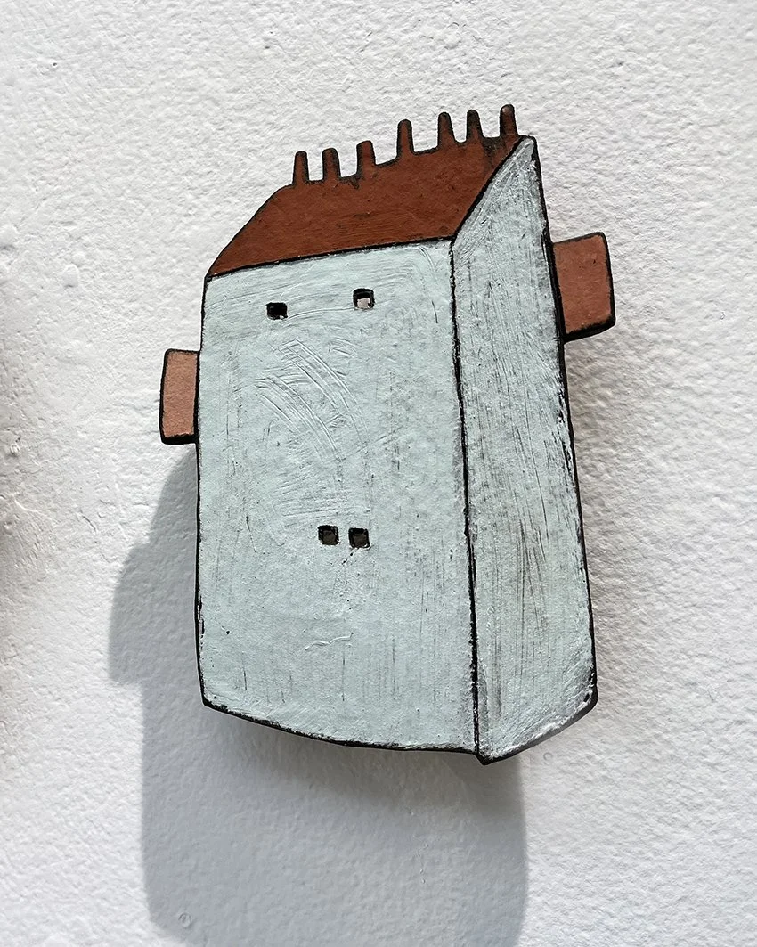 ett Keramikhus, målat i blått vitt och brunt, monterat på en vit vägg.