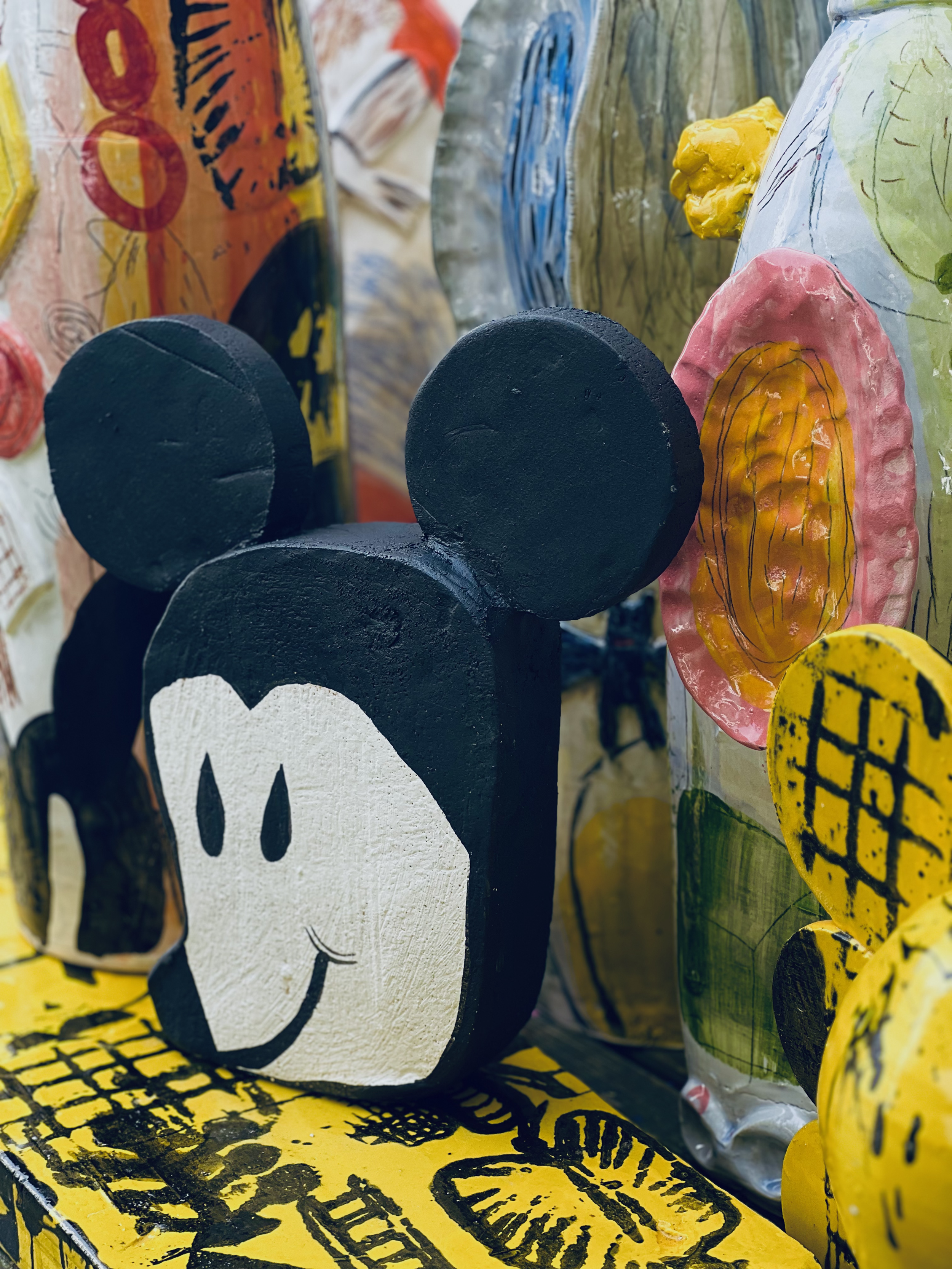  konstnärligt målat och skulpterat material med en Mickey Mouse-figur i fokus, omgiven av färgglada, abstrakta konstverk.