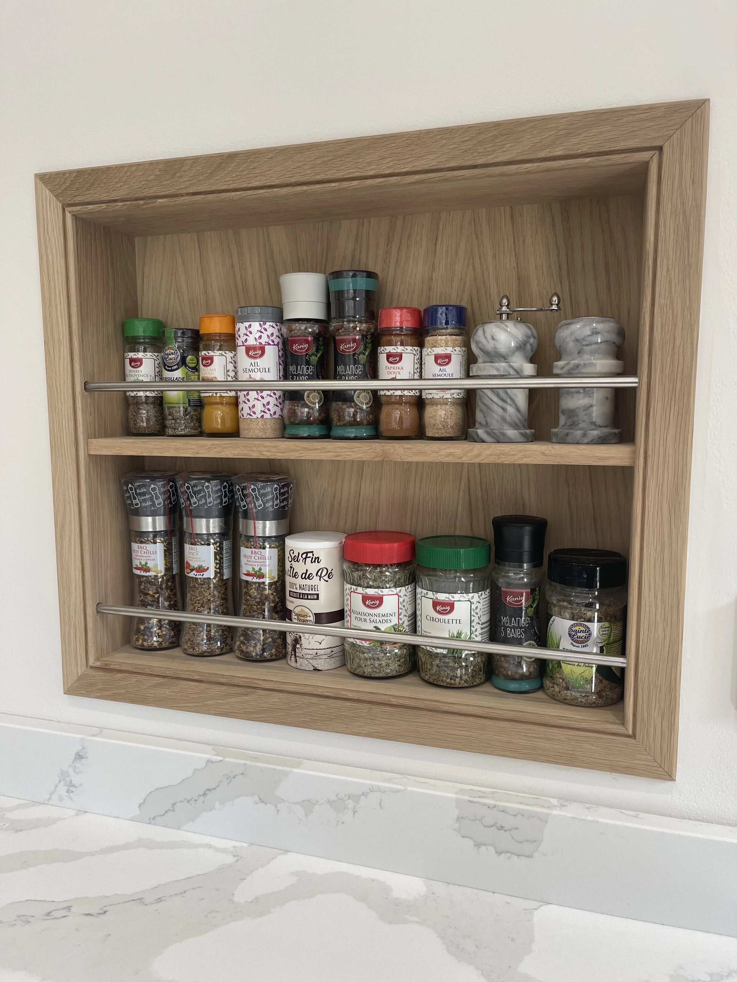 Bespoke oak pice rack with various spice jars and shakers on a white marble countertop.