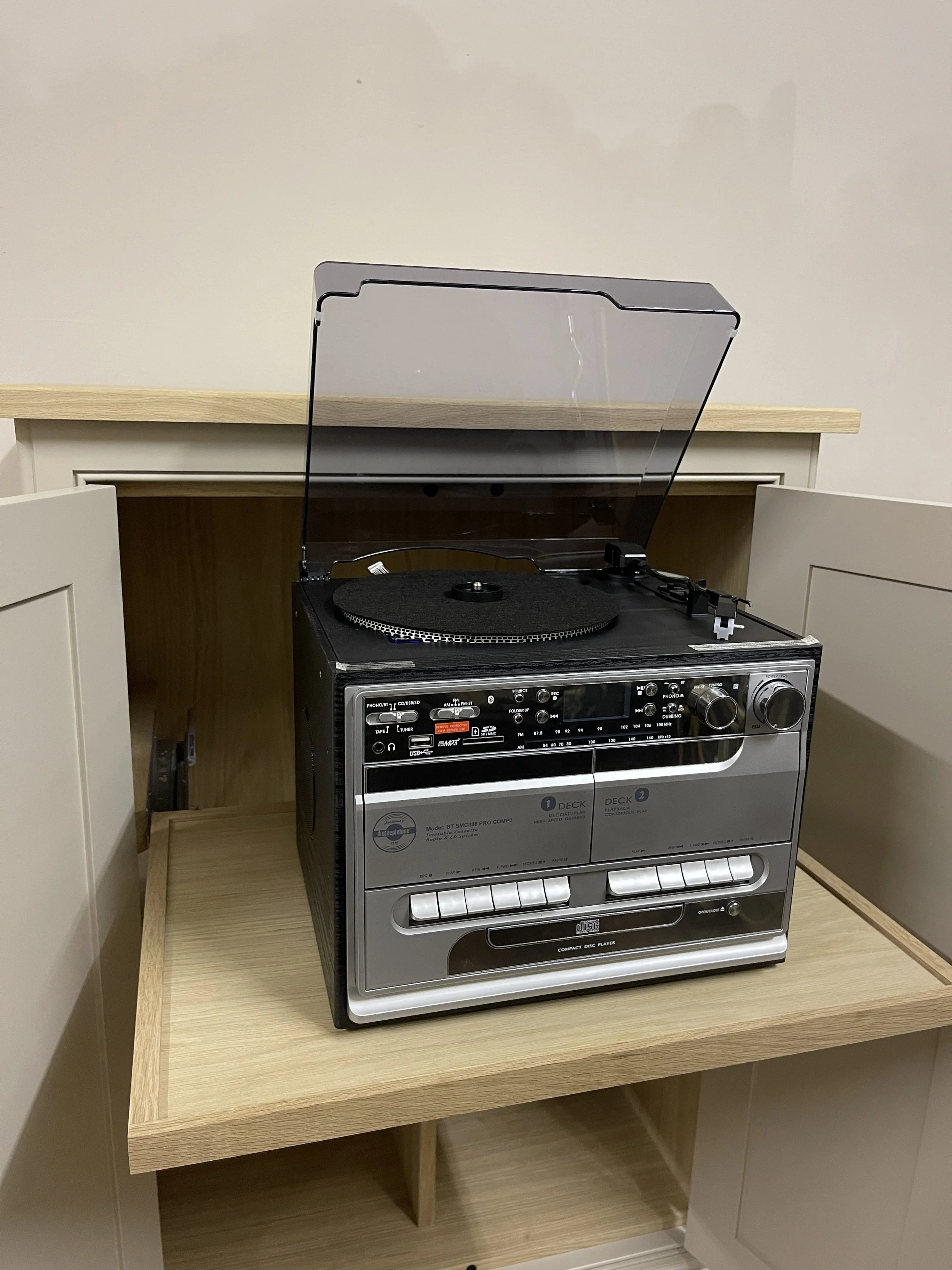 Retro turntable and cassette player combo open on a wooden shelf with a transparent lid.