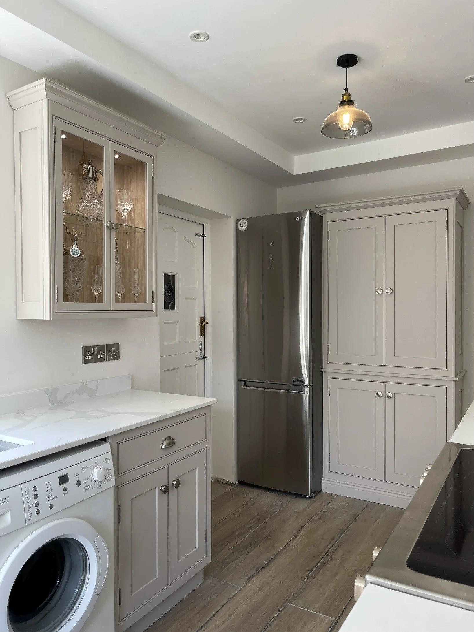 Bespoke kitchen cabinetry with light grey cabinets, stainless steel refrigerator, marble countertop, and pendant light.