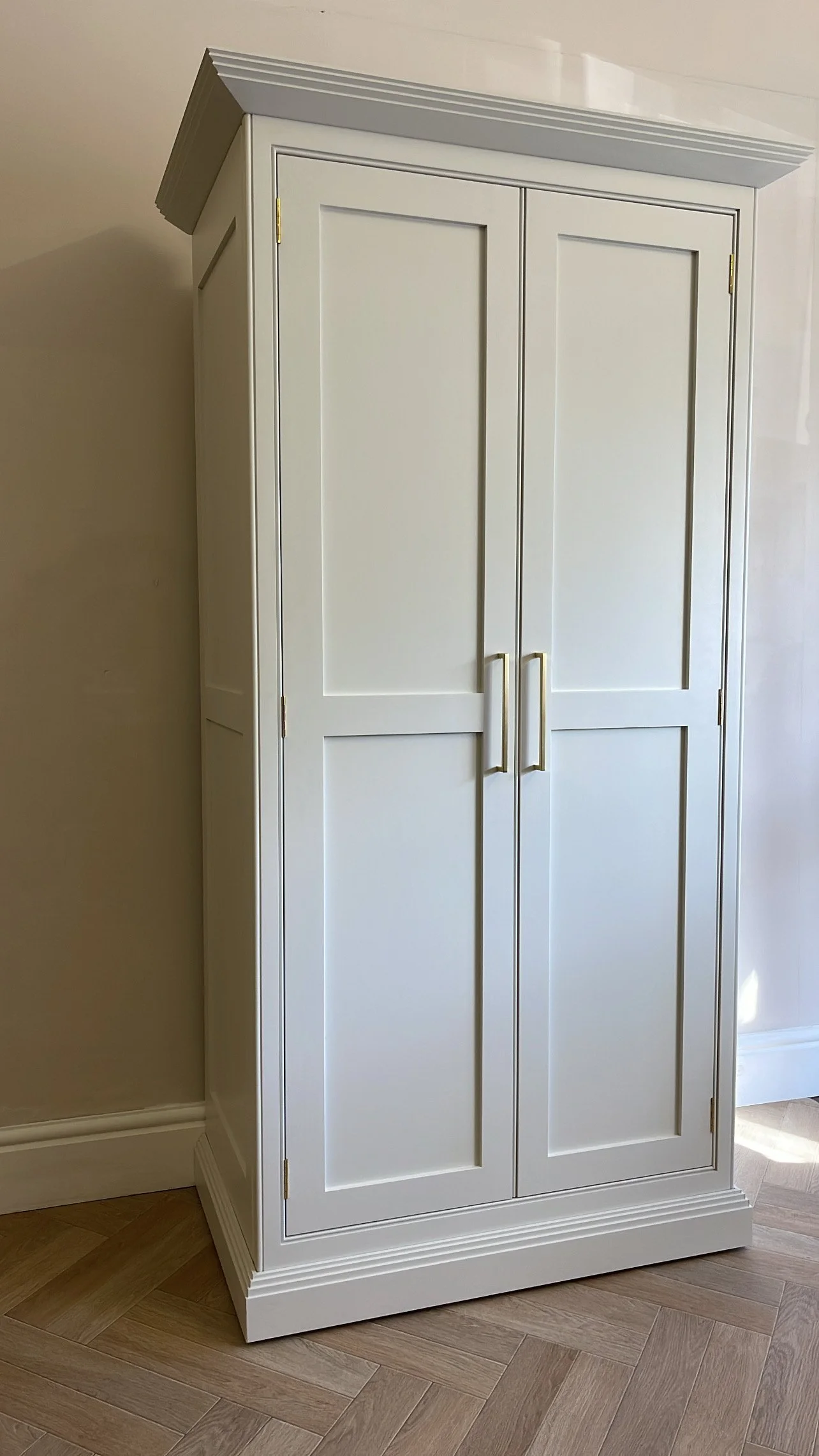 Handmade kitchen/pantry cupboard with two shaker style doors and brass handles in a room with herringbone wooden flooring.
