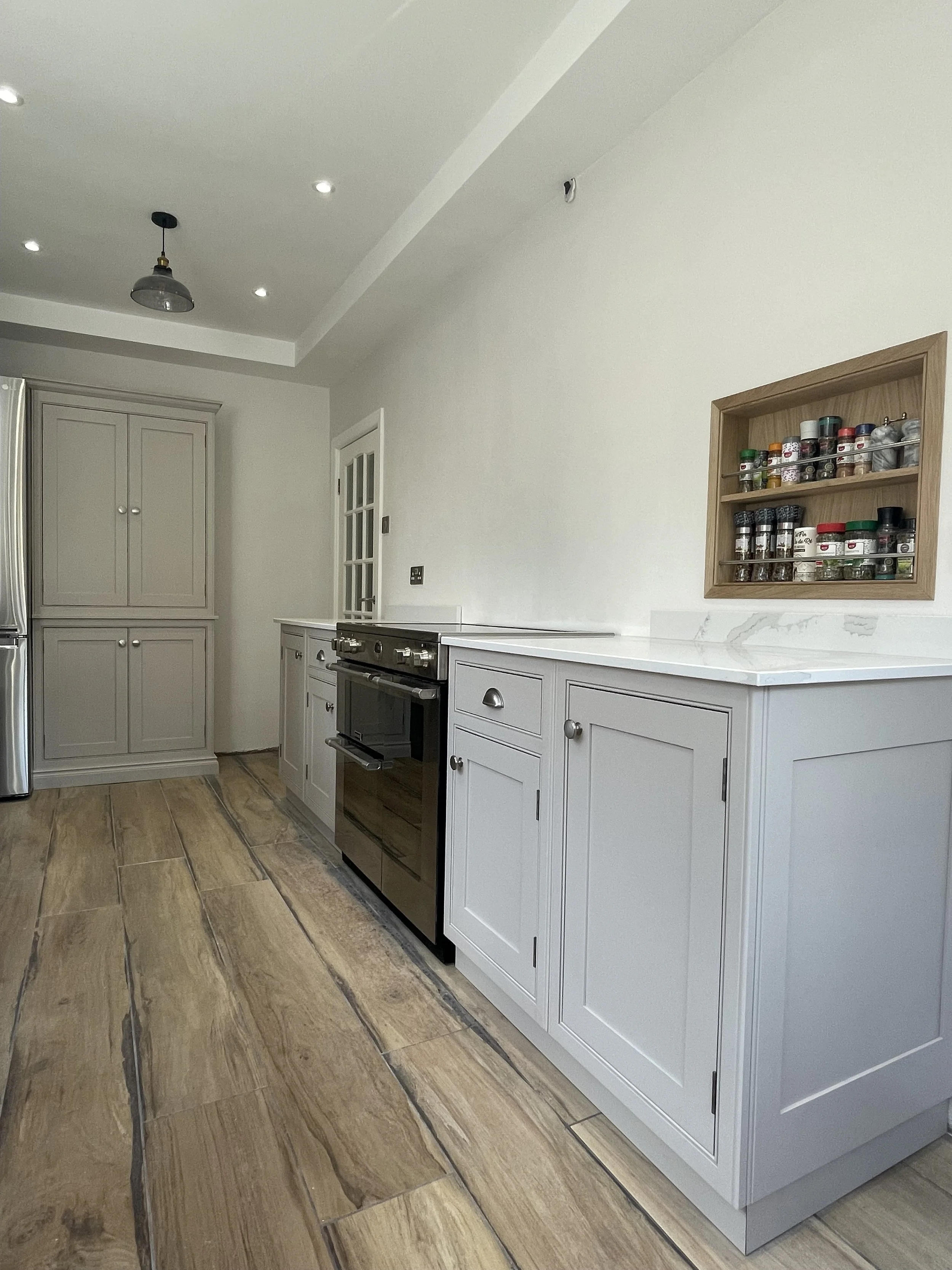 Bespoke cabinetry with hand painted cabinets, wooden flooring, stainless steel appliances, and bespoke fitted wall-mounted spice rack.