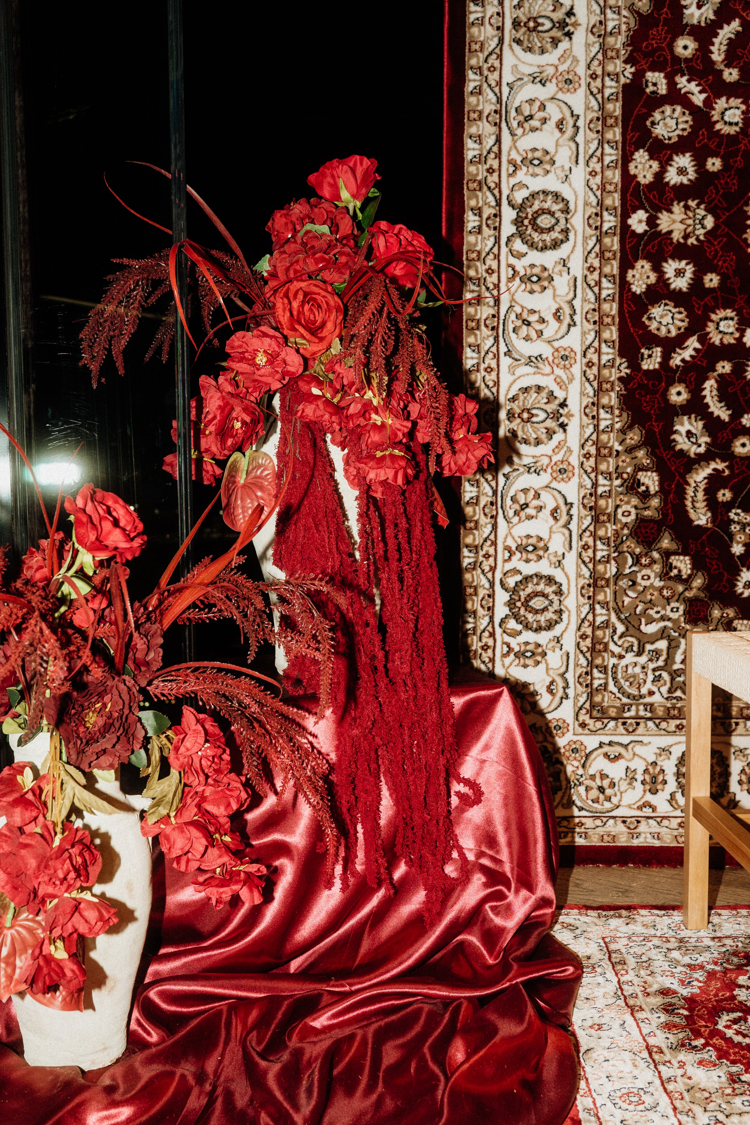 Rote Blumen und Textilien in einer Dekoration, mit Teppichen im Hintergrund.