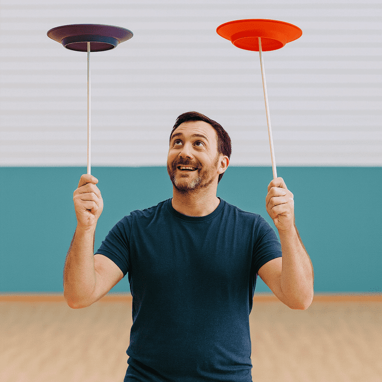 Adult man spinning two plates at a corporate circus skills team building workshop in the UK.