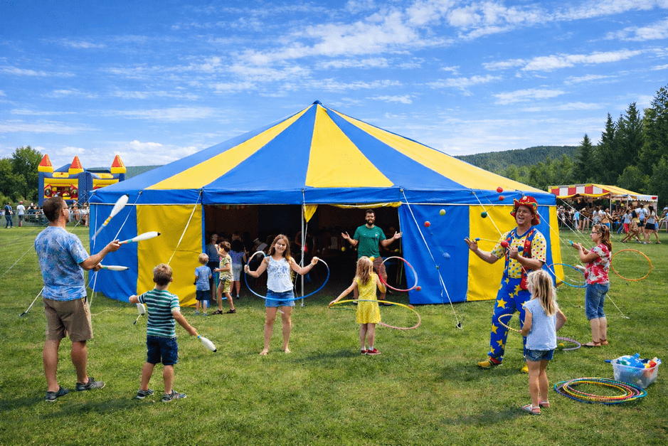 Blue and yellow circus big top tent hire with children and performers doing circus skills workshops outside at a UK event.