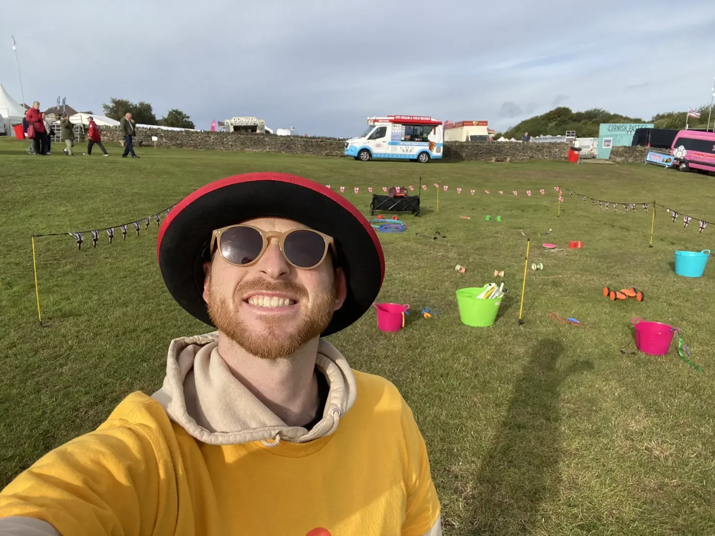 Young male Elevate Circus Workshops performer in yellow t-shirt and black bowler hat smiling at a UK festival