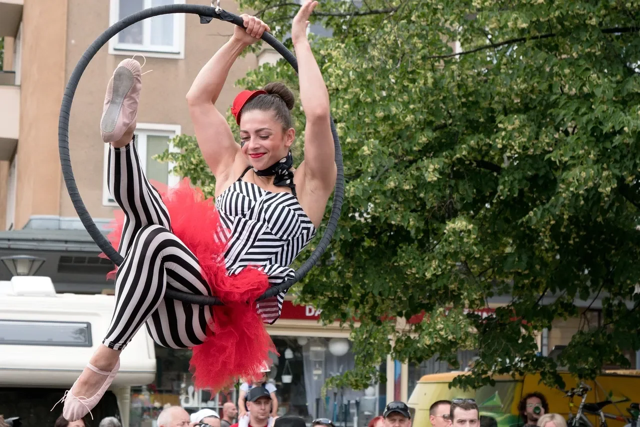 an aerial hoop artist balancing in the inside of a hoop dressed in a stripy black and white leotard red ballet tutu and tiny red bowler hat