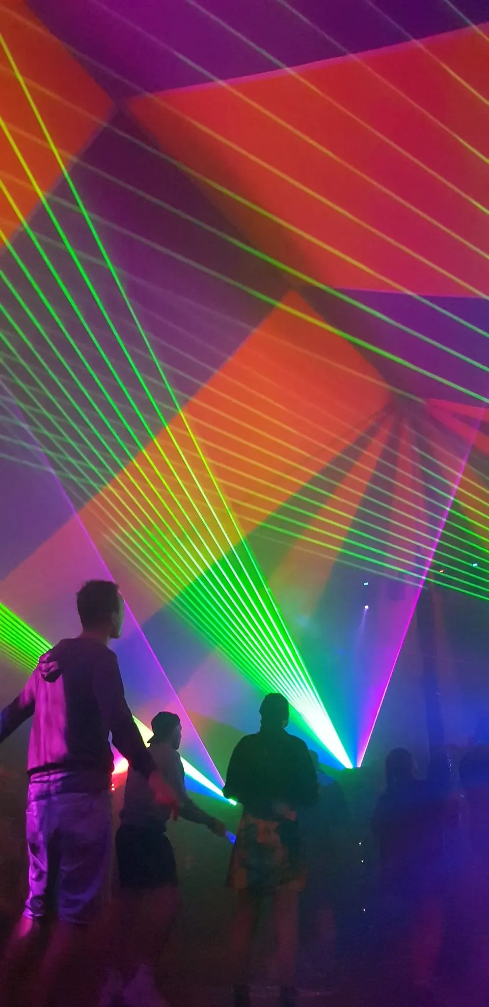People dancing in side a blue and yellow tent with colorful laser lights in green, purple, orange, and pink.