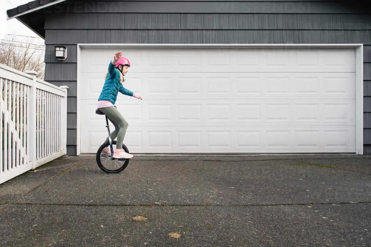 girl balancing on unicycle on driveway in front of garage