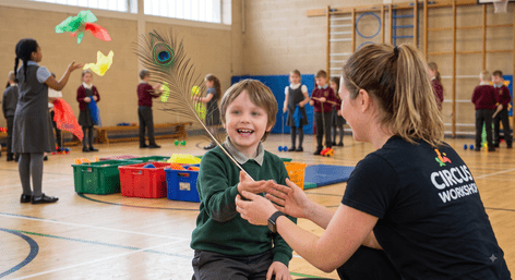 A boy interacting with a teacher while holding a large feather during an SEN circus skills workshop at school.