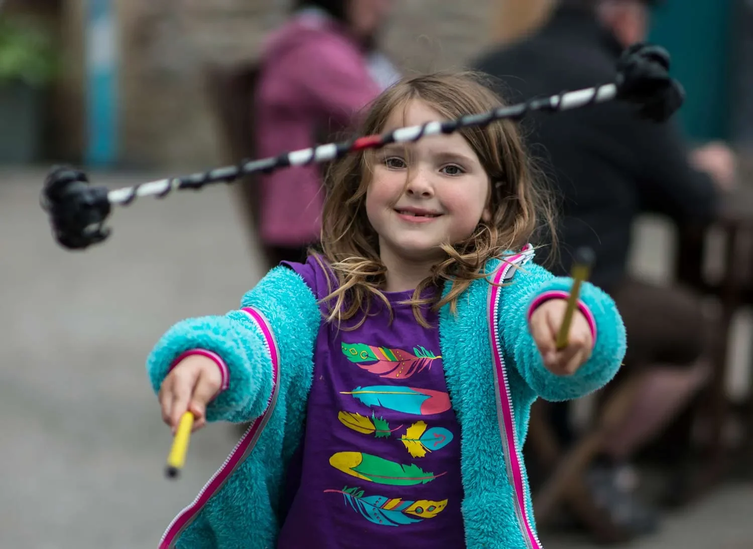a young girl in a purple tee shirt and turquoise fleece hoodie playing with flower sticks