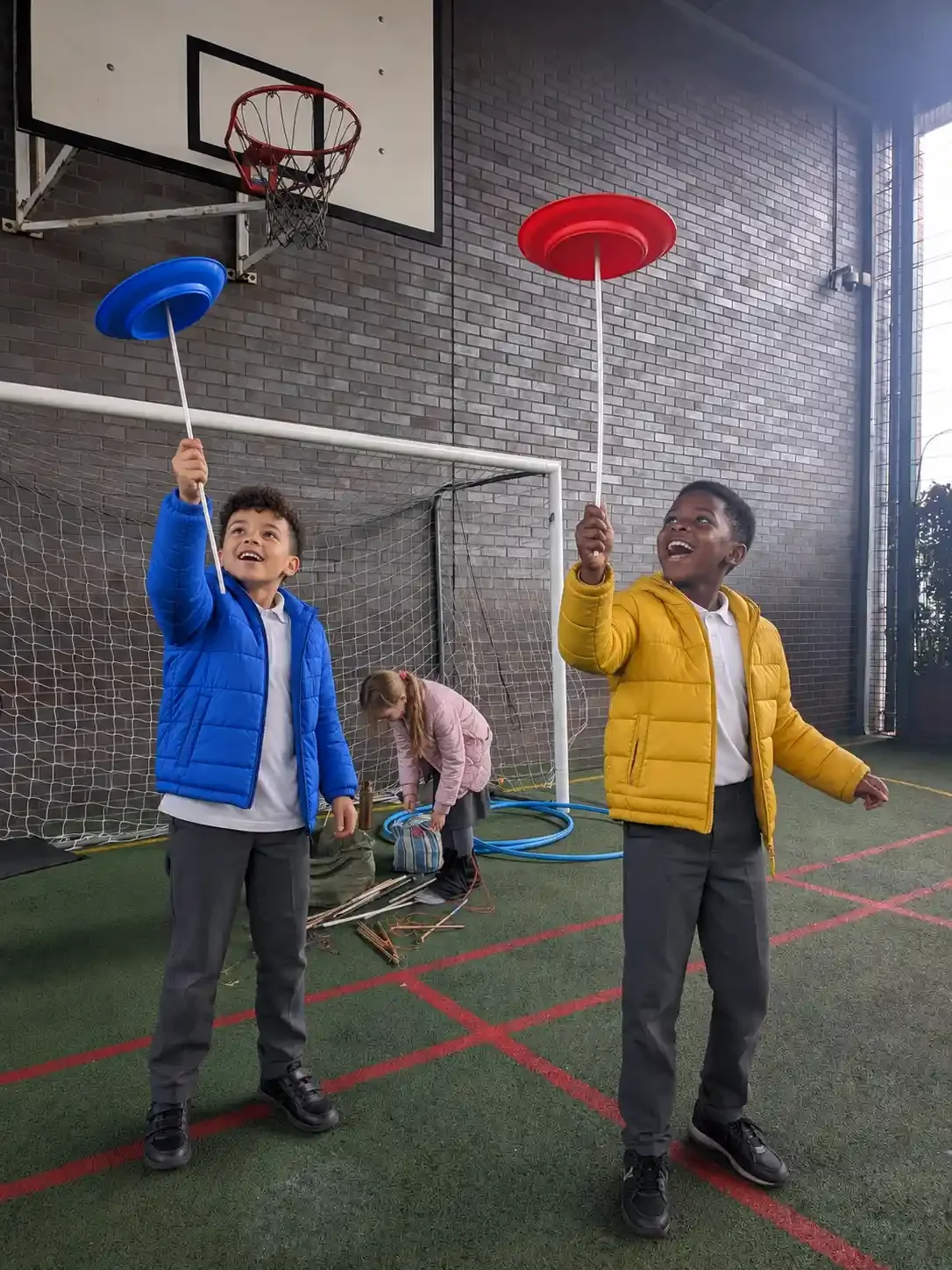 2 children enjoying a circus skills workshop in an indoor MUGA area