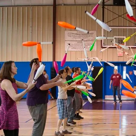 a group of adults in a gymnasium practicing juggling with clubs