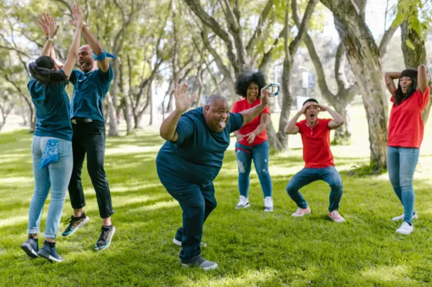 A group of 6 adults in a park playing a game and jumping around happily