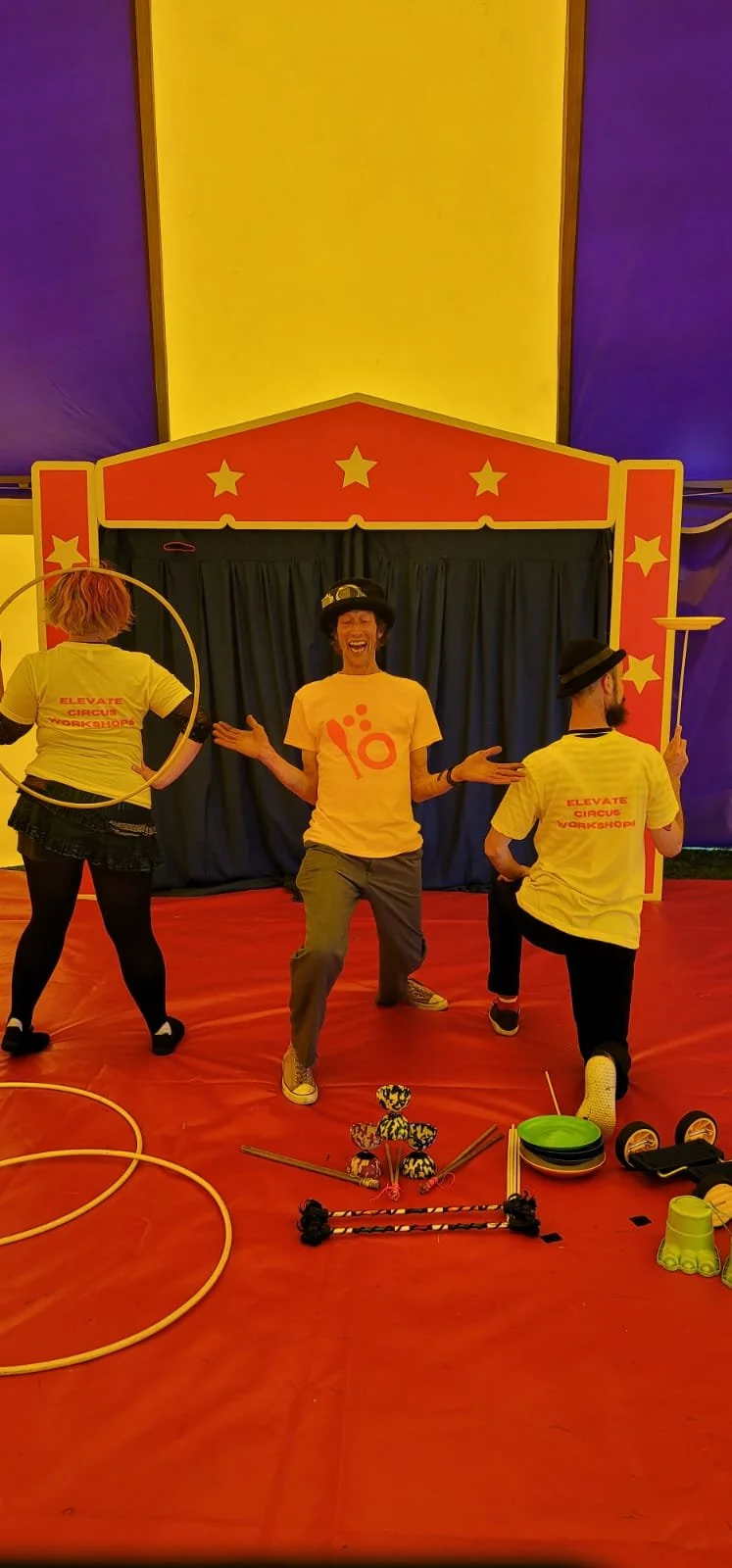 Three Elevate Circus Workshops performers in yellow branded t-shirts and bowler hats performing inside a purple and yellow big top circus tent