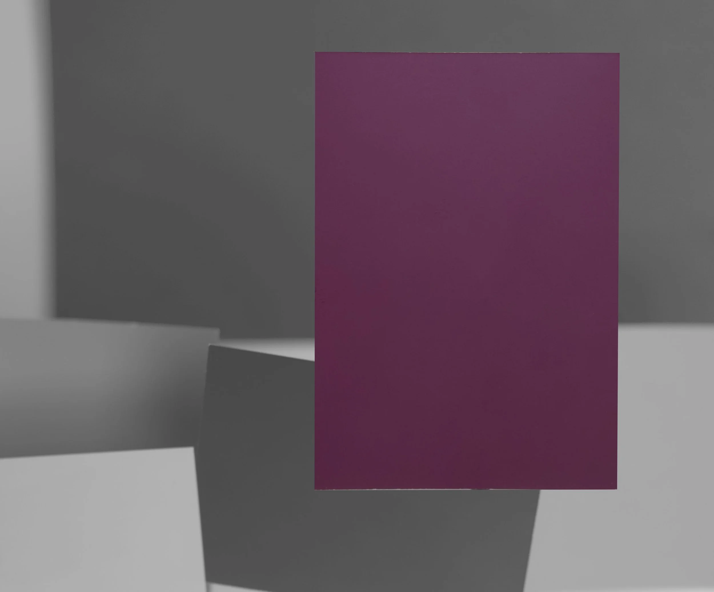 A pink rectangular sheet of paper standing upright on a surface, with gray and white background walls.