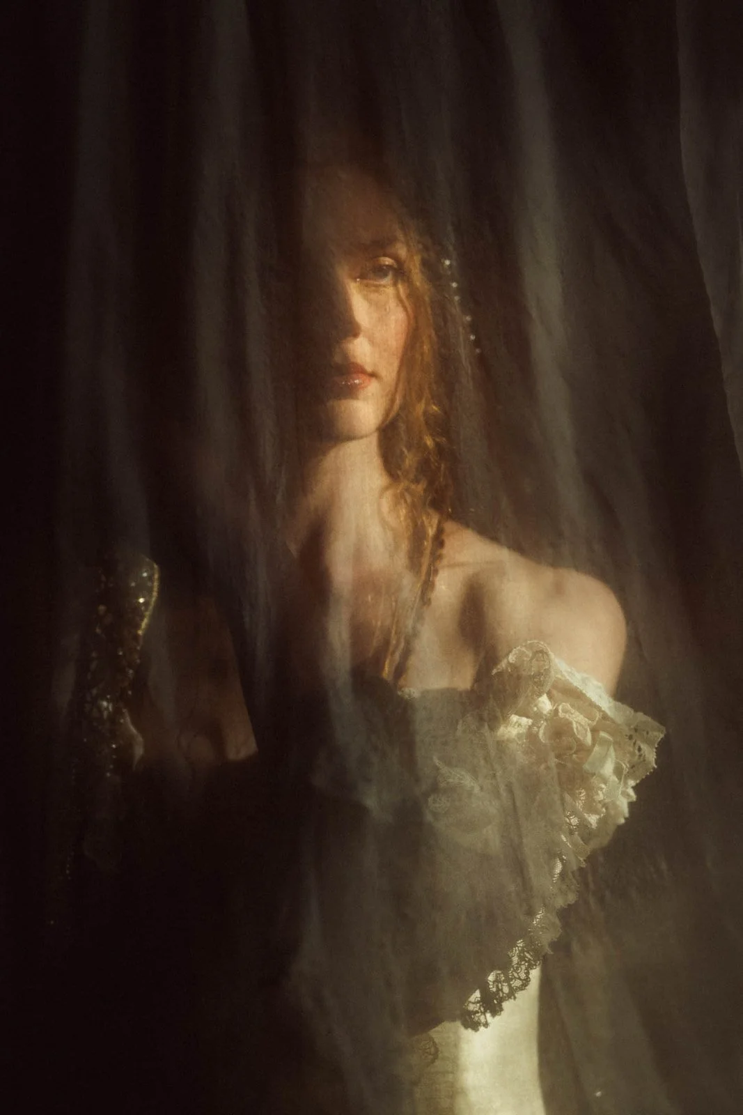 Une femme avec des cheveux roux, portant une robe en dentelle, vue à travers un voile noir.