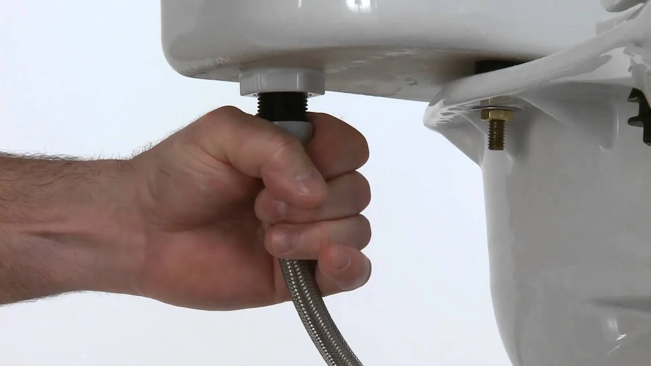 A person tightening a bolt under a sink using a wrench.
