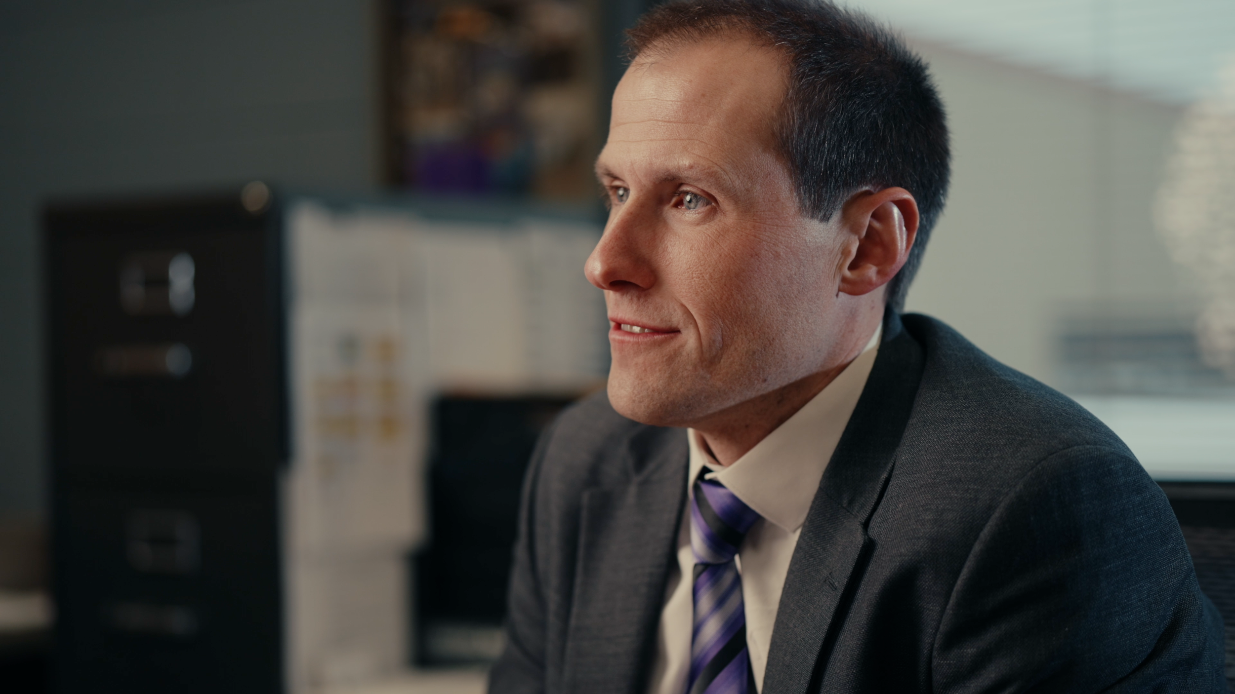 Close-up of a man in a suit and tie looking to his right in an office setting.