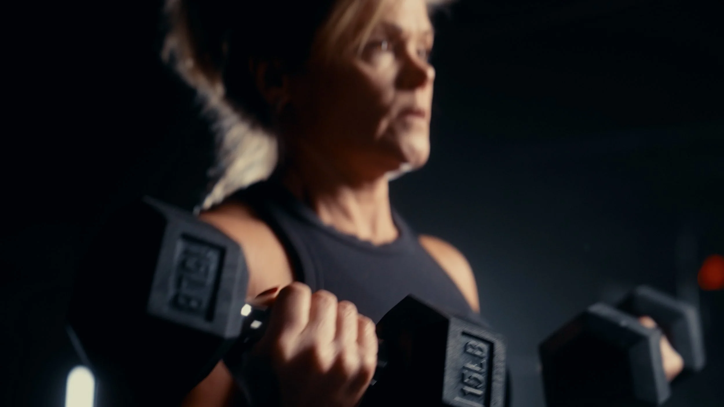 A woman lifting dumbbells during a workout in a gym.