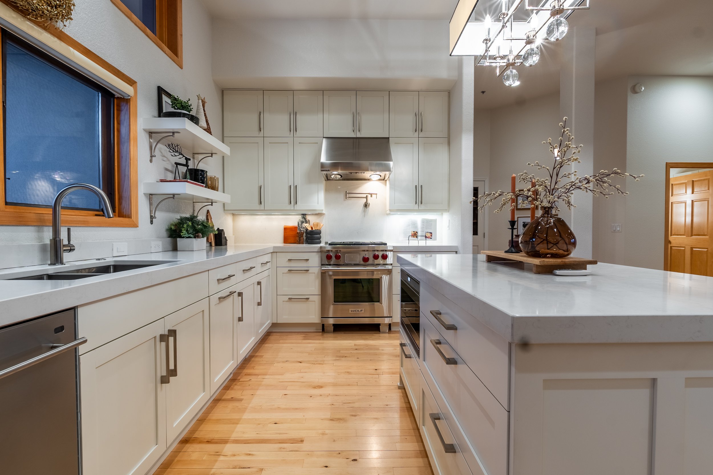 Modern kitchen with white cabinetry, stainless steel appliances, hardwood floors, and a large island with decorative centerpiece.