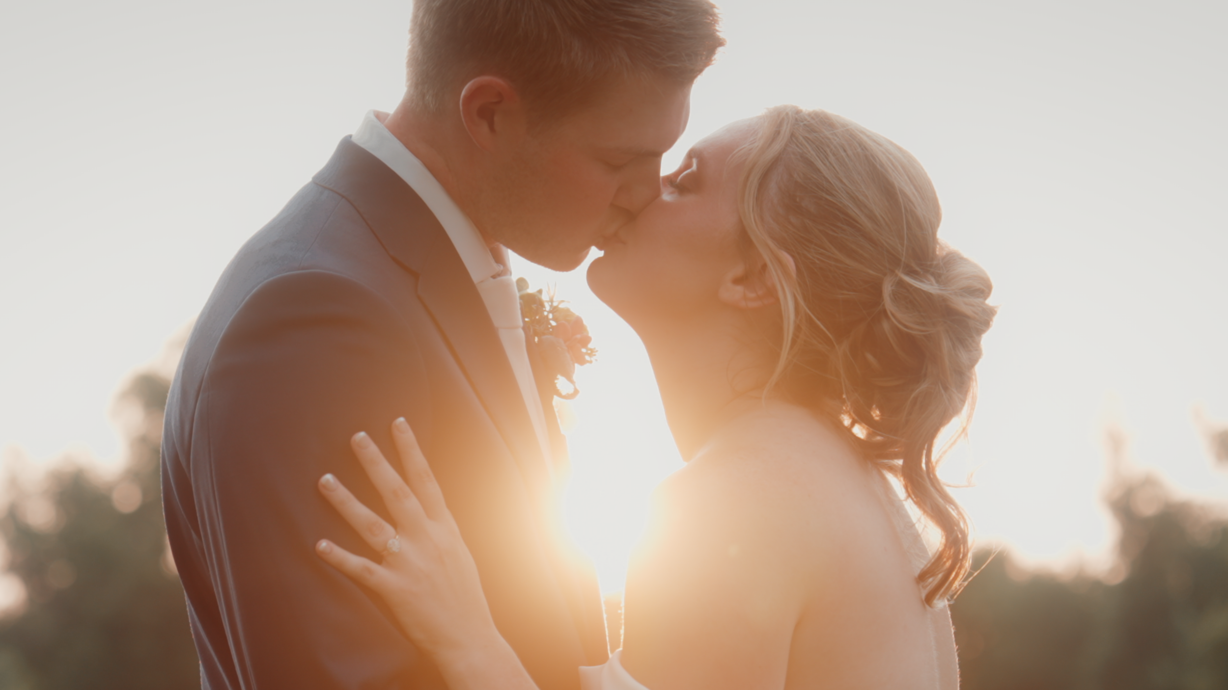 A bride and groom sharing a kiss at sunset, with the sun behind them creating a warm glow.