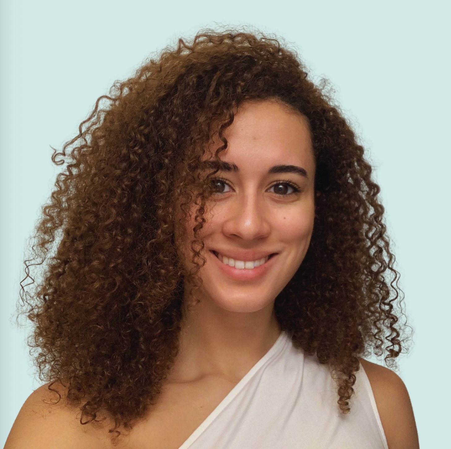 A young woman with curly brown hair and a bright smile. She is wearing a sleeveless white top against a light blue background.