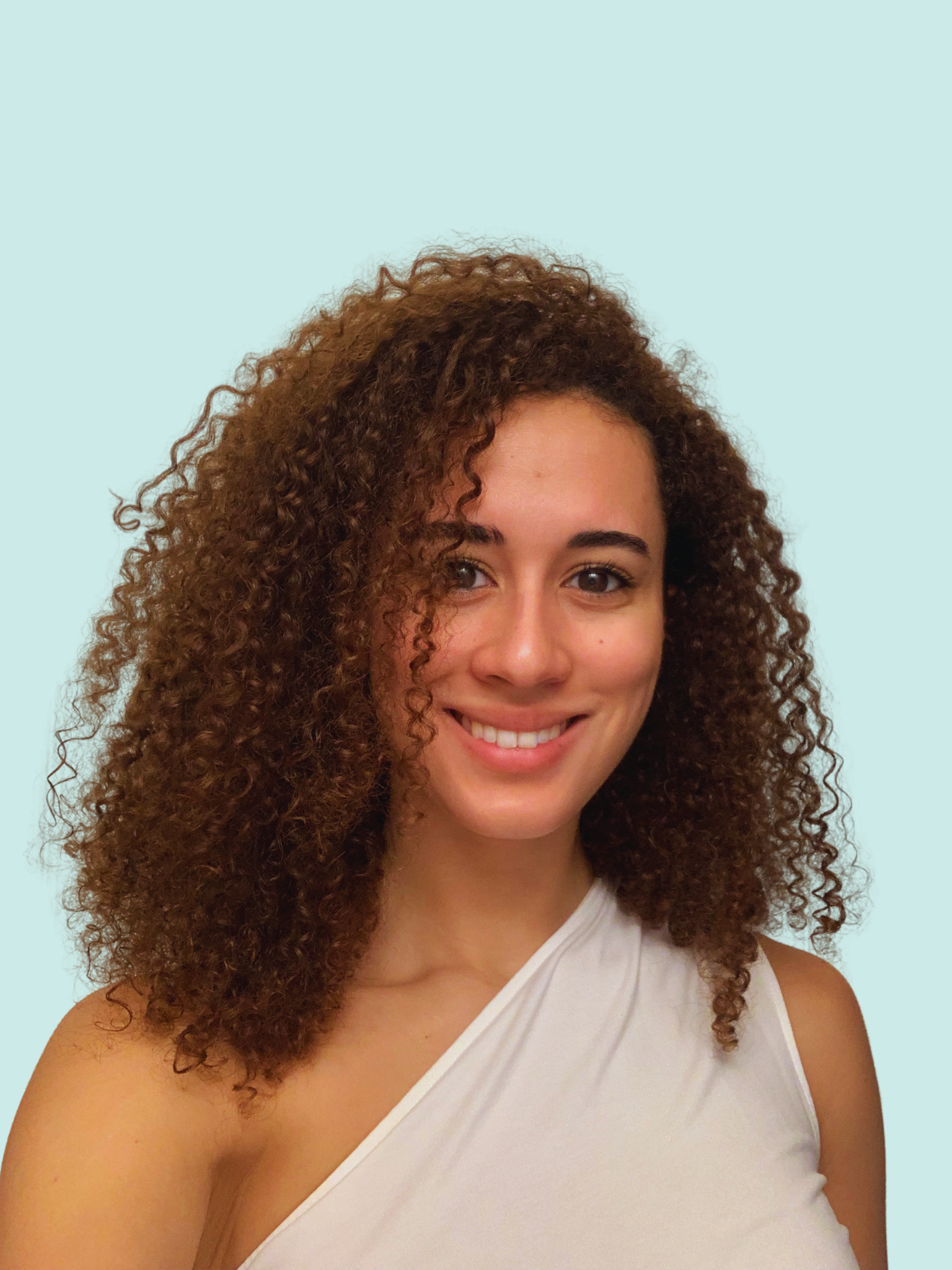 Close-up of a woman with curly brown hair, smiling, wearing a white sleeveless top, against a light blue background.