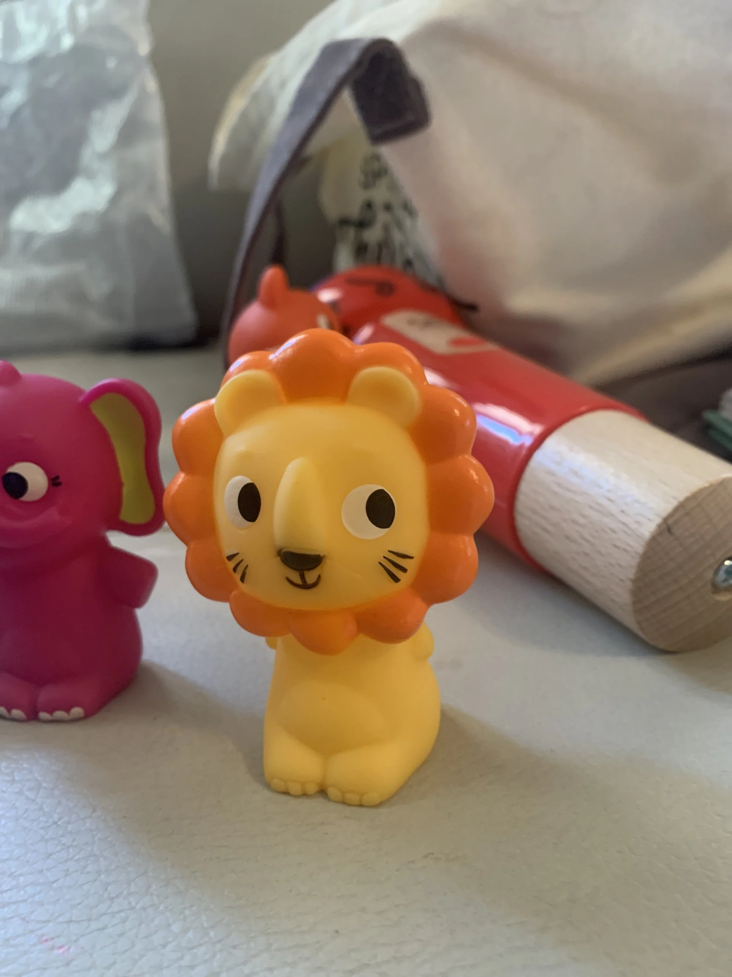 Colorful plastic lion and hippopotamus toys on a light surface, with other toys and objects in the background.
