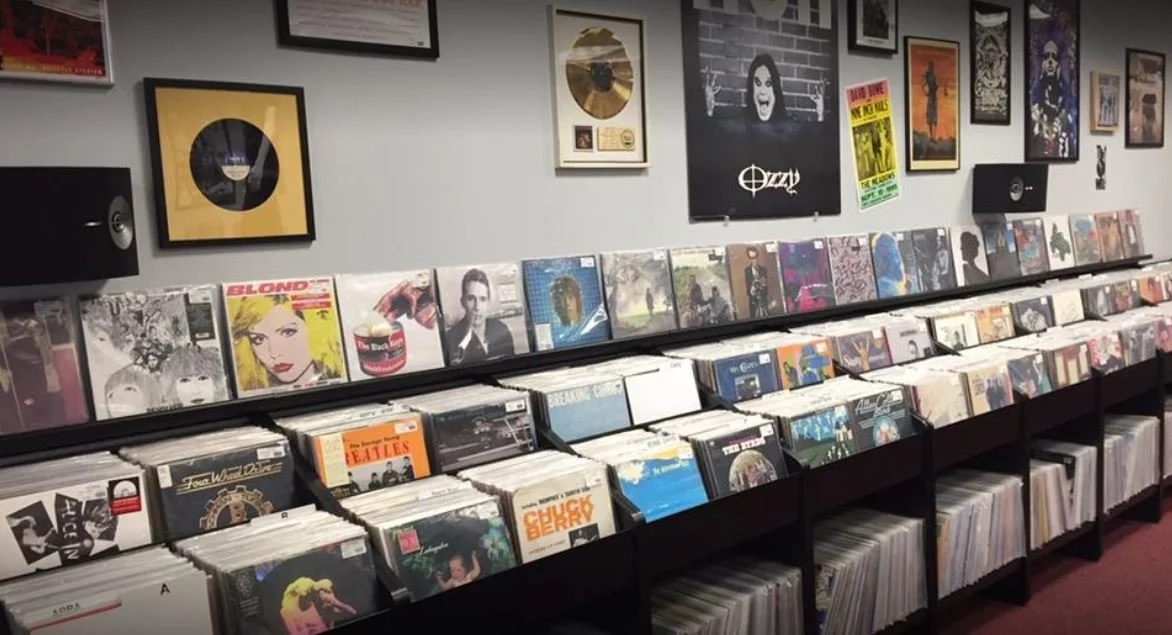 A wall of framed music awards and posters with shelves filled with vinyl records.