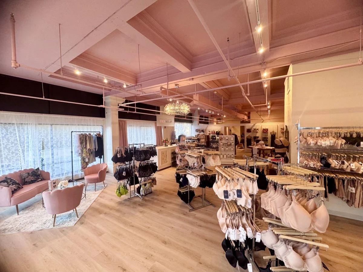 Interior of a boutique clothing store with racks of lingerie, clothing, and a cozy seating area with pink chairs and velvet pillows.