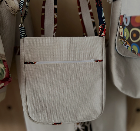 White shoulder bag with a front zip pocket, hanging among other bags.