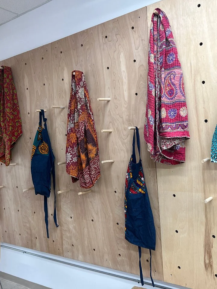 Colorful scarves and bags hanging on hooks on a light wood pegboard wall.