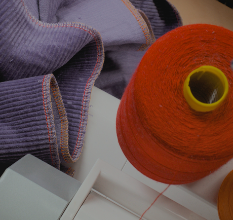 Close-up of a spool of orange thread and a piece of purple fabric on a white surface.